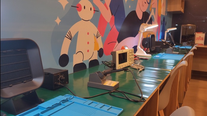 Lab bench with a soldering station and oscilloscope in front of a colourful mural