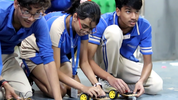 Students in blue uniforms assembling small robot cars on the floor