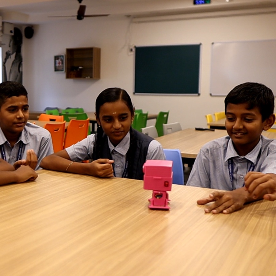 Students working with a small pink robot at a classroom table